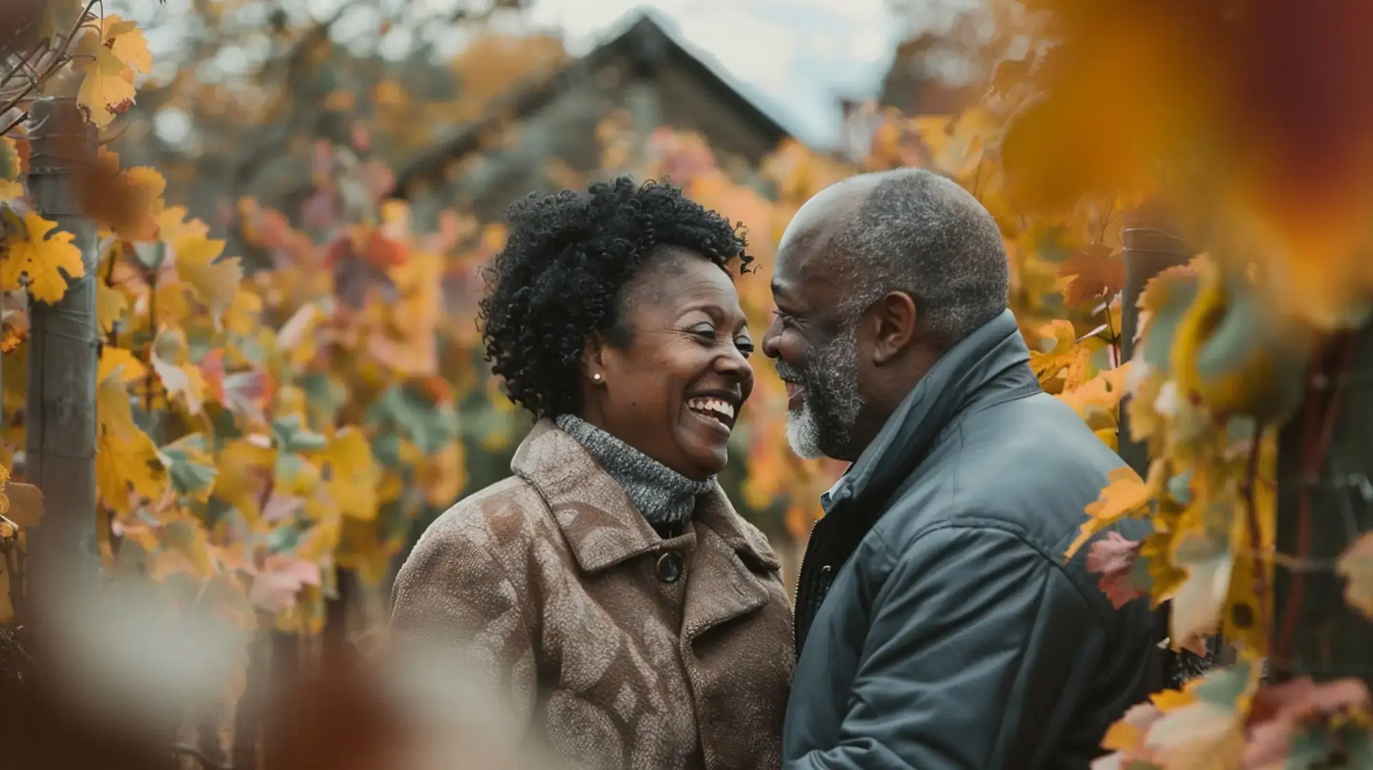 Older couple smiling at each other while walking through autumn leaves outdoors