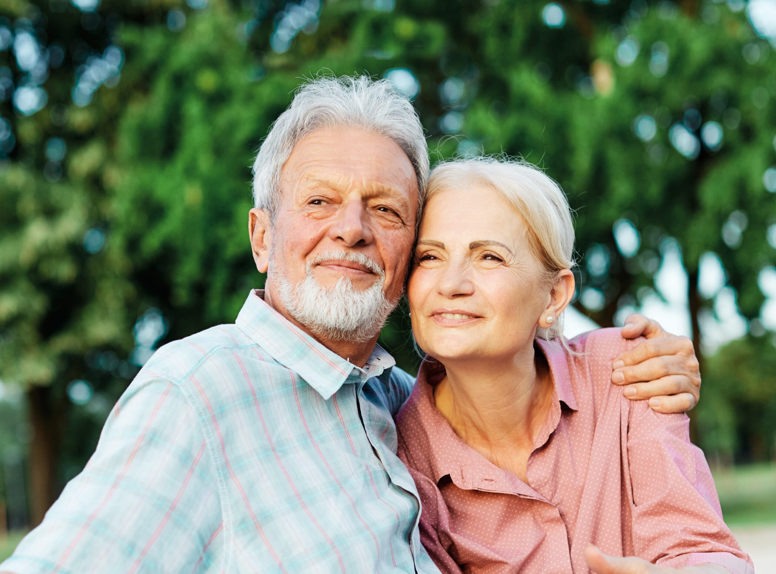 Senior couple outdoors, smiling closely together with arms around each other